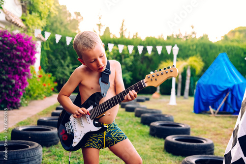 Young boy plays a piece to the electric guitar  very concentrated in his interpretation  dressed in a swimsuit.