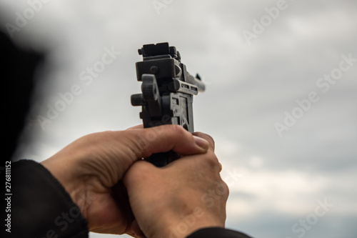Hand with a gun against the sky, clouds. Life-size weapons mockup. Summer evening.