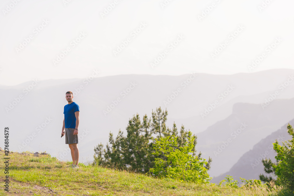 A fit male athlete is preparing for a work out in nature while looking over a cliff at the large lake and mountain line.