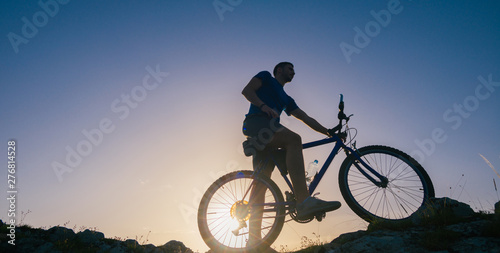 Silhouette of a fit male mountain biker riding his bike uphill on rocky harsh terrain on a sunset.