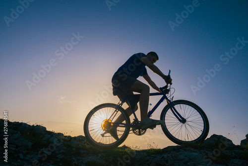 Silhouette of a fit male mountain biker riding his bike uphill on rocky harsh terrain on a sunset.