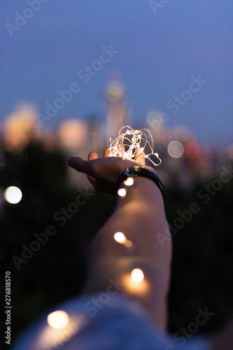 String lights on hand in front of cityscape