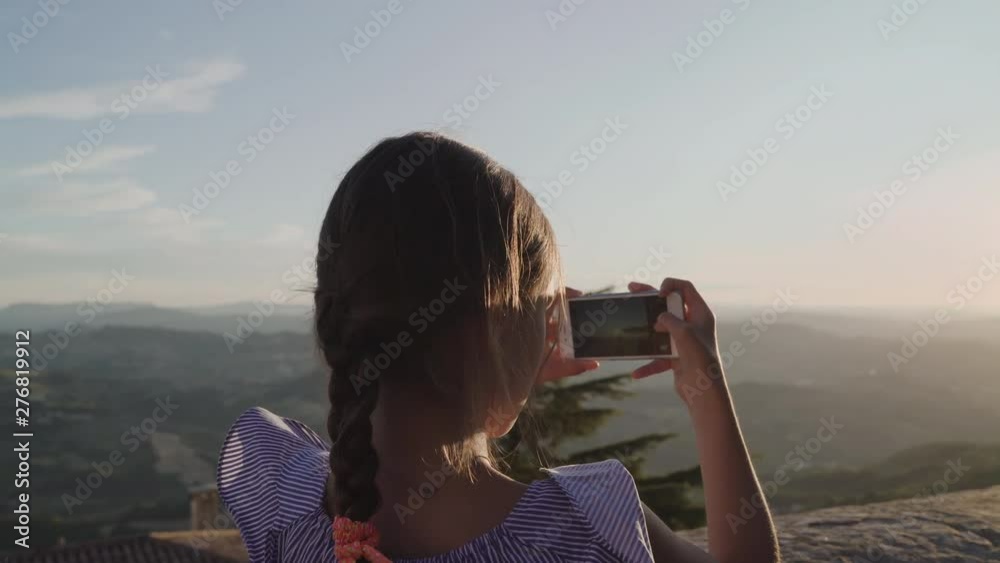 Little girl child take photos of mountains by smartphone camera at sunset. San Marino, Italy Little girl child take photos of mountains by smartphone camera at sunset. San Marino, Italy