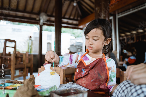 child painting ceramic pot with paint brush in pottery workshop