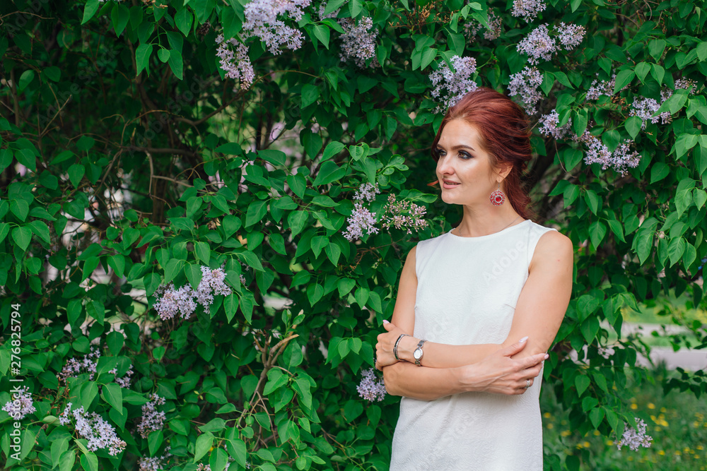 Charming woman wearing beautiful white dress standing next to lilac bush. Copy space. Charming woman wearing beautiful white dress standing next to lilac bush. Copy space.