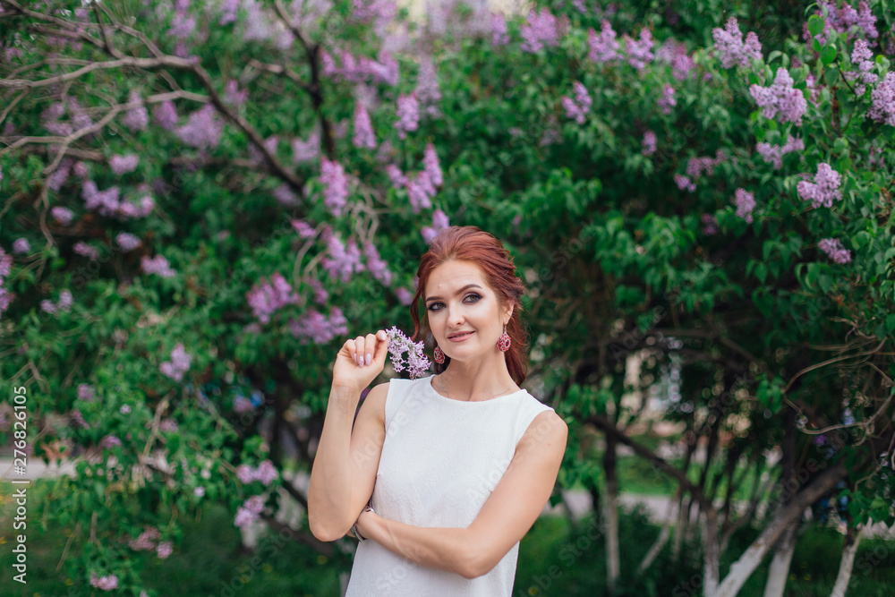Charming woman wearing beautiful white dress standing next to lilac bush. Copy space. Charming woman wearing beautiful white dress standing next to lilac bush. Copy space.