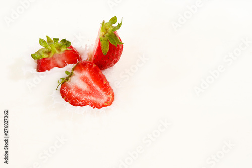 Red natural ripe strawberries falling into milk cream