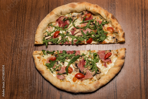 top view two halves of pizza with arugula, ham, and tomatoes