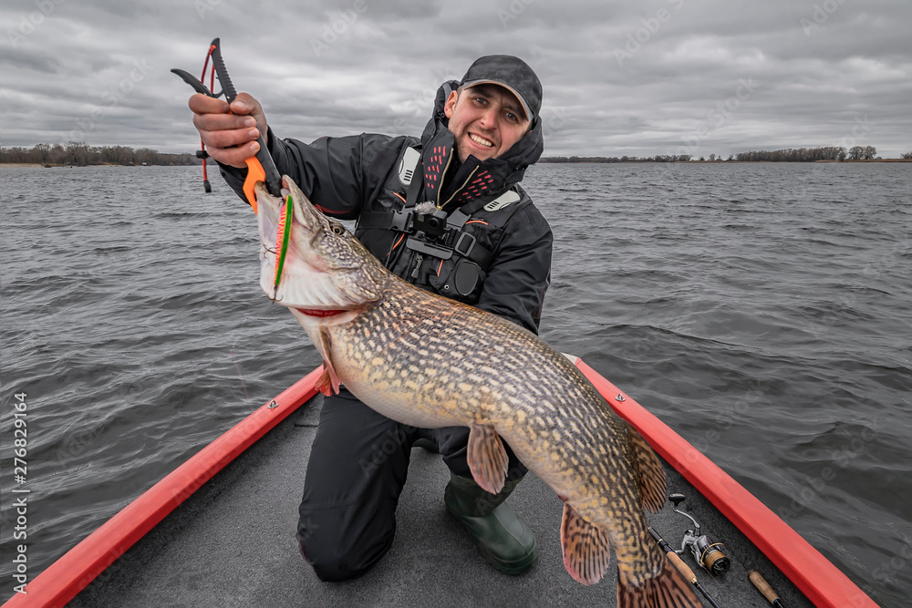 Pike fishing. Happy fisherman with big fish trophy at the boat with tackles Pike fishing. Happy fisherman with big fish trophy at the boat with tackles