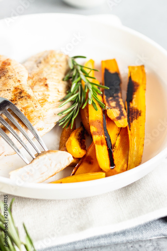 Grilled chicken or turkey fillets (steaks), roasted carrots and rosemary on a white plate, gray stone background.