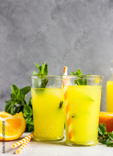 Orange lemonade in glass with fresh orange and mint over light grey stone table. Refreshing summer drink. Cocktail bar background concept. Copy space.