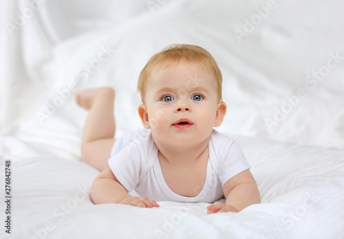 Tableau sur toile Portrait of a charming blue-eyed baby 7 months in bed in white clothes