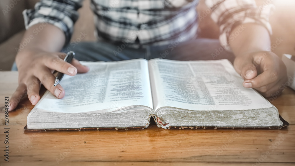 Naklejka premium Close up Bible or book with a man reading at home. christian concept.