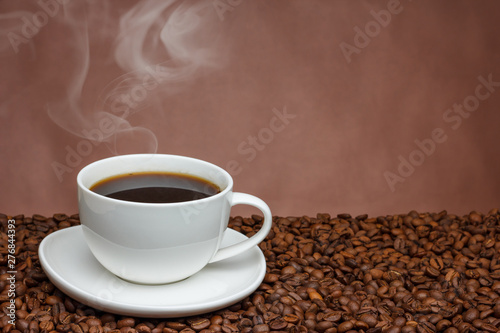 white cup of coffee with steam on a brown background on coffee beans