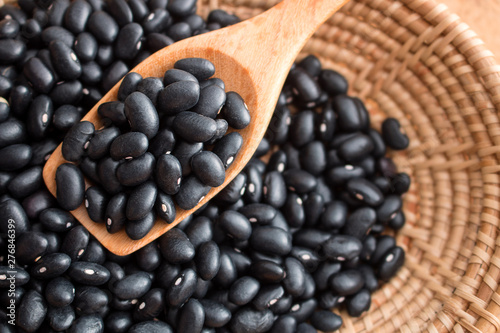 Raw black beans in basket and spoon on wood table.