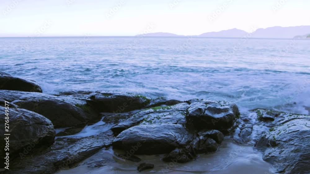 slow motion of some waves hiting rocks in the cost during a sunny and beautiful day in a break spot slow motion of some waves hiting rocks in the cost during a sunny and beautiful day in a break spot