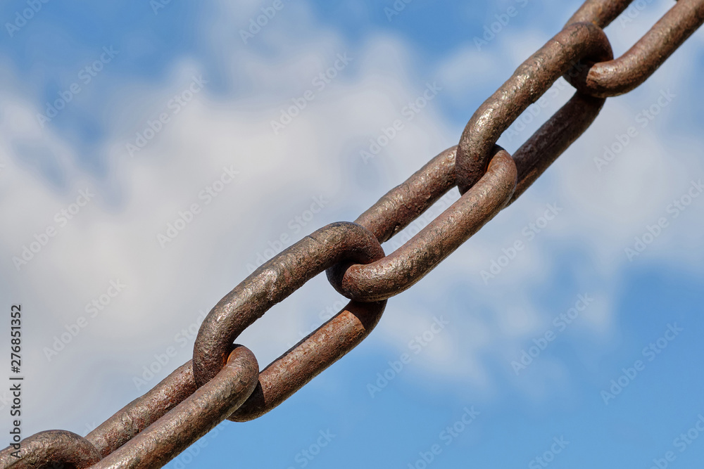 An old rusty chain on a blue background. In the background is blue sky with white clouds. An old rusty chain on a blue background. In the background is blue sky with white clouds.