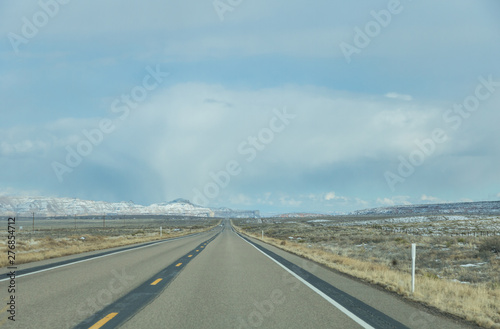 Straight road ahead with overcast sky above snowcapped mountain in Utah, USA