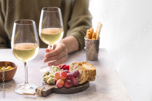 Woman holding glass of white wine in the restaurant. Different snacks, Blue cheese, olives, baguette slices and cured meat. Tasting party lifestylebackground.