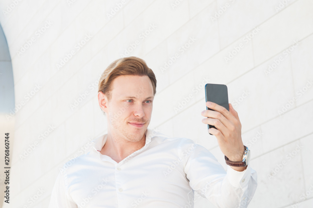 Smiling business man taking selfie photo outdoors. Guy posing and standing with building wall in background. Selfie concept. Front view. Smiling business man taking selfie photo outdoors. Guy posing and standing with building wall in background. Selfie concept. Front view.