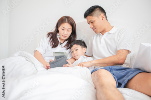 family and son watching and  play tablet on bed