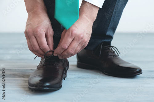 Man is tying shoelaces on his brown leather shoes on a blue wooden floor background.