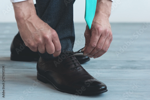 Man is tying shoelaces on his brown leather shoes on a blue wooden floor background.