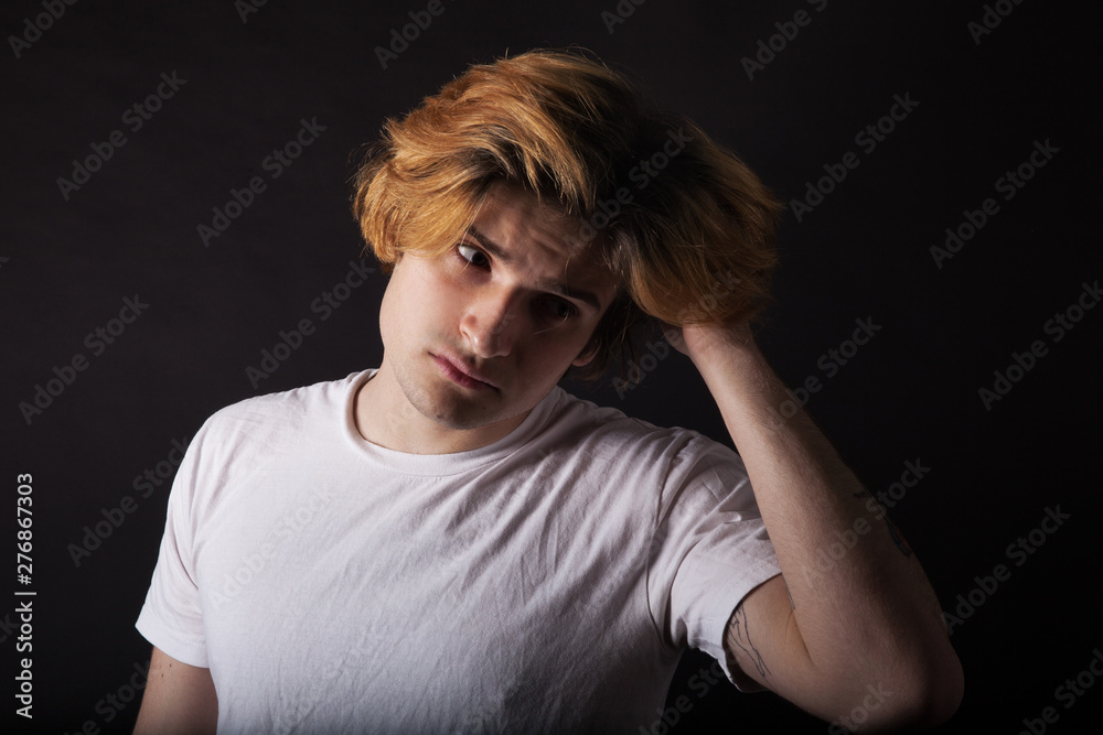 Young caucasian adult with dyed blonde hair posing on black