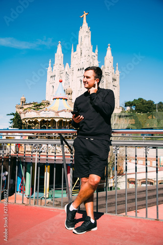 Young handsome man talking on the phone via earbeans standing on the barcelona streets. Summer vocation. photo