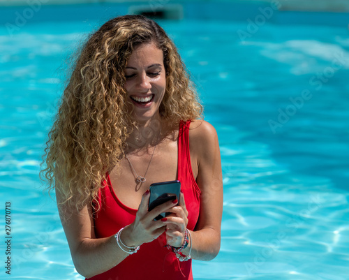 Blonde girl uses mobile phone inside the pool.