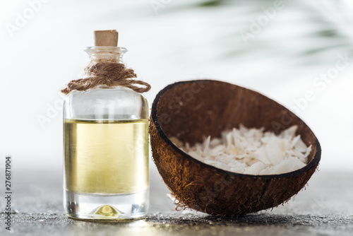 selective focus of bottle with coconut oil near coconut shell with coconut shavings