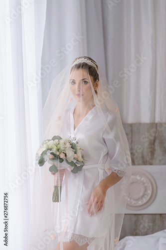 Bride portrait in a dressing gown before the wedding ceremony. The bride is covered with a veil.