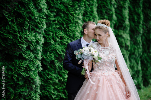 Bride and groom hugging against a green wall in the park