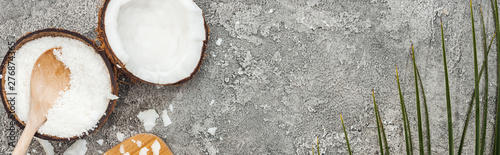 top view of coconut halves and flakes on grey textured background with copy space, panoramic shot