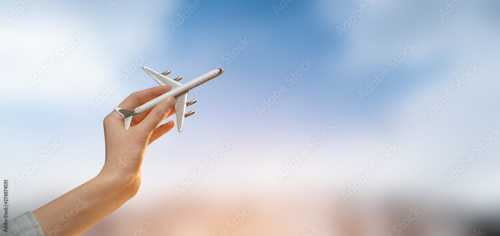 Hand holding a plane over blurred city background with sky.Tourism or travel concept - obrazy, fototapety, plakaty 