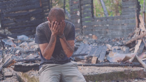 Portrait of a sad man on the background of a burned house, after fire . Consequences of fire disaster accident. Ruins after fire disaster, despair concept. photo