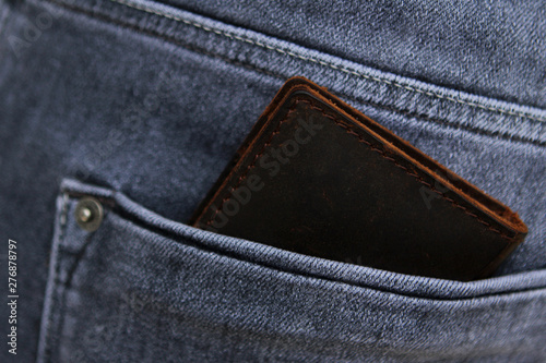 Dark brown men's wallet made from high-quality genuine leather lies in the back pocket of men's gray jeans