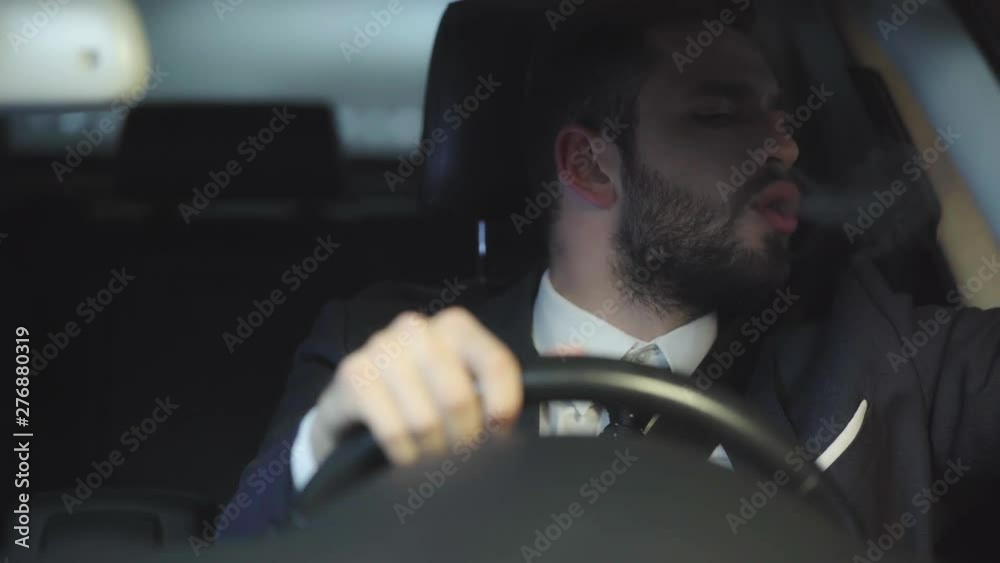 selective focus of handsome man in suit smoking while driving car 
