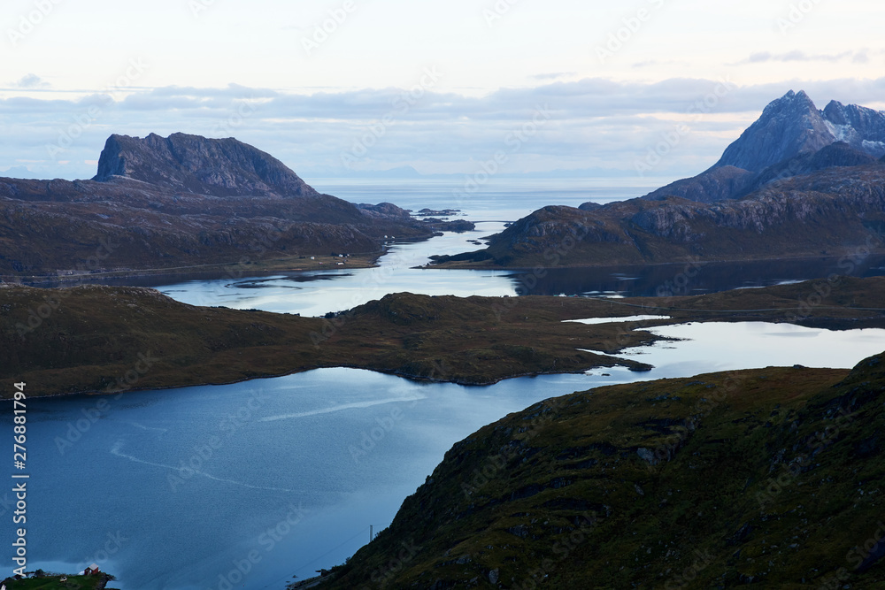 View from above over a bay with snowcapped mountains during evening blue hour on Lofoten Islands in Norway. View from above over a bay with snowcapped mountains during evening blue hour on Lofoten Islands in Norway.