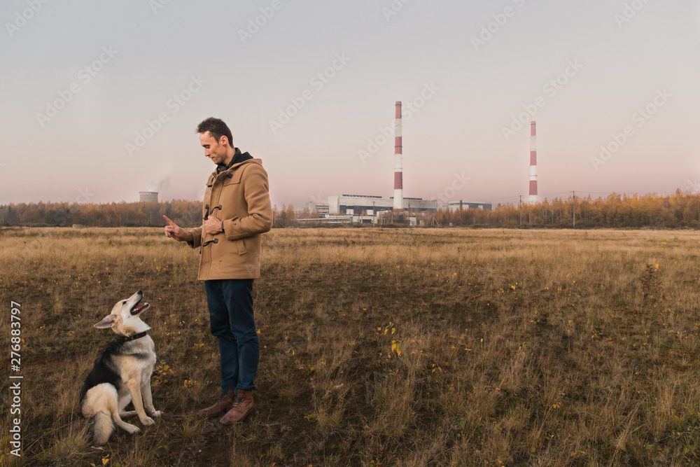 A man with a mongrel dog walking on autumn meadow