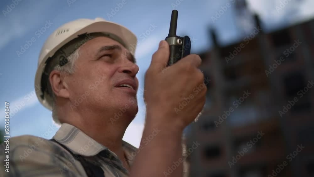 Senior engineer builder using a walkie talkie at a construction site. Sunset time. Slow motion