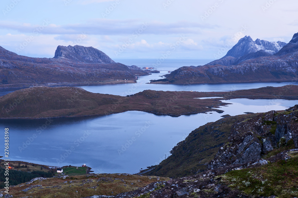 View from above over a bay with snowcapped mountains during evening blue hour on Lofoten Islands in Norway. View from above over a bay with snowcapped mountains during evening blue hour on Lofoten Islands in Norway.