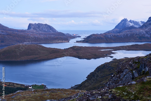 View from above over a bay with snowcapped mountains during evening blue hour on Lofoten Islands in Norway.