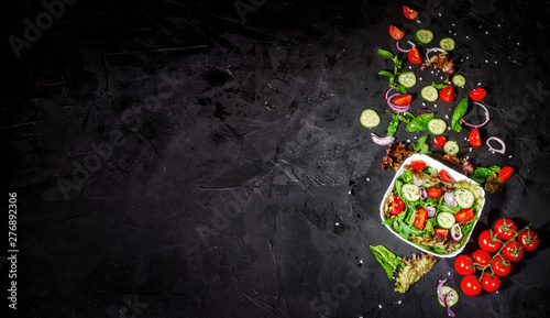 Foto Various fresh mix salad leaves with tomato and cucumber in a glass bowl on dark background with ingredients