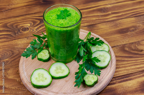 Glass of green detox smoothie of cucumber and parsley on a wooden table