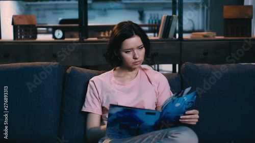 attentive young woman reading journal while sitting on couch at home photo