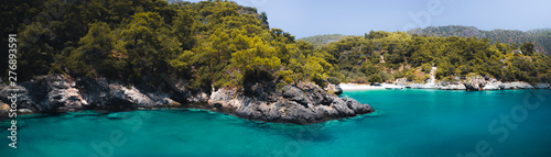 Secluded beach surrounded by valley cliffs in a tranquil bay with turquoise water and sailing boats at sunrise, Oludeniz, Turkey panoramic