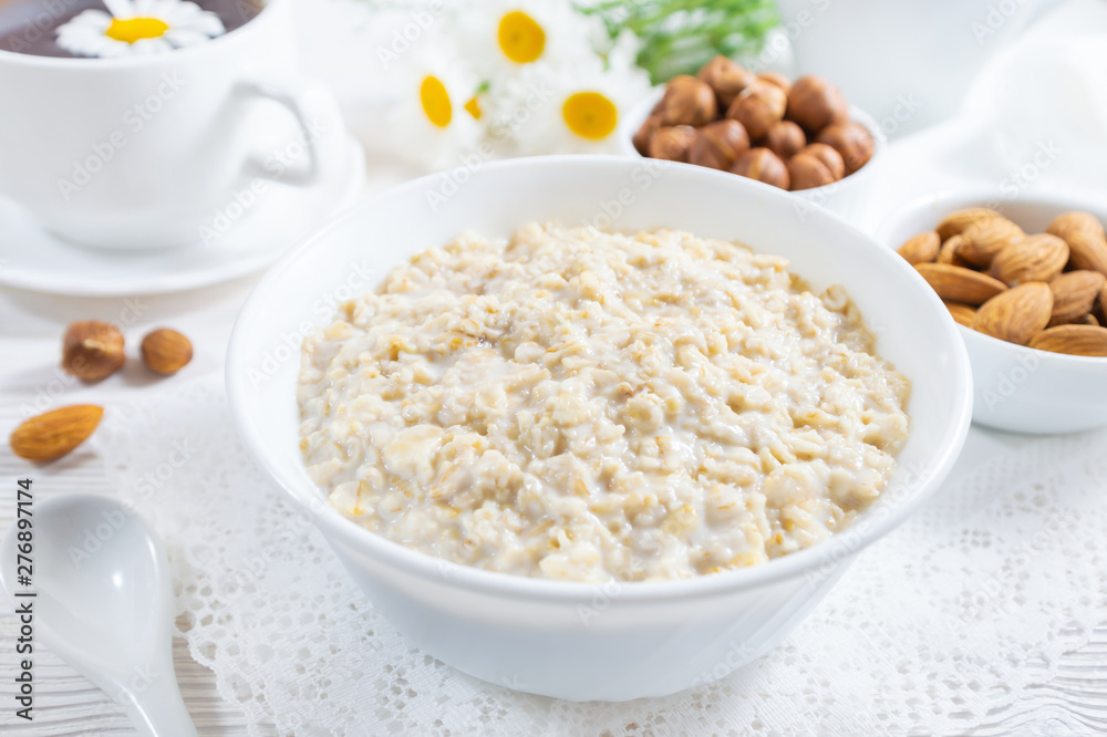Oatmeal with nuts in bowl on white wooden table. Oatmeal with nuts in bowl on white wooden table.