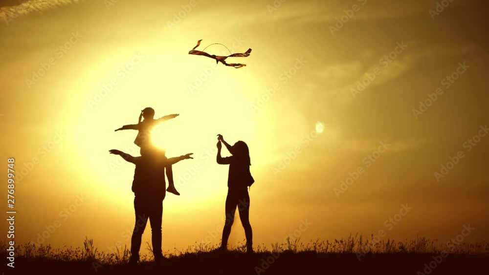 Happy family playing with a kite while on meadow, sunset, in summer day. Funny family time. Happy little girl launch a kite with parents. Mom, Dad and daughter are happy together. Happy family playing with a kite while on meadow, sunset, in summer day. Funny family time. Happy little girl launch a kite with parents. Mom, Dad and daughter are happy together.
