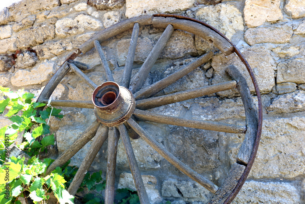  An old wooden wagon wheel on background of stone wall